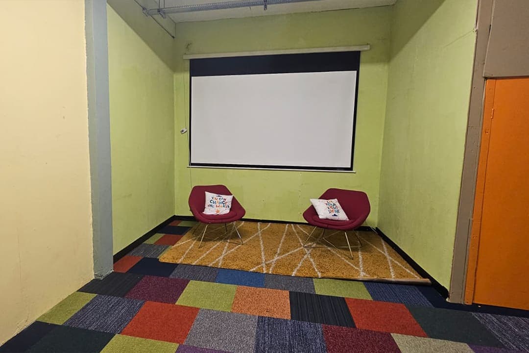 The Creative Breakout Space with a colourful patterned carpet, red armchairs and a projector screen.